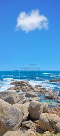 Foto de Rocas en la orilla de una playa con majestuoso océano a través del horizonte. Copyspace en el mar con fondo de cielo azul y costa rocosa en Camps Bay, Sudáfrica. Paisaje tranquilo y pintoresco para unas vacaciones de verano. - Imagen libre de derechos