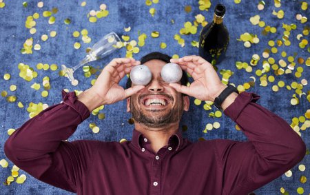 Photo for Christmas, drunk and funny with a man on the floor, laughing during a party or celebration event from above. Comic, comedy or festive with a happy young male person holding decorations over his face. - Royalty Free Image