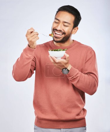 Photo for Health studio, happy man and eating salad, vegetables or green food meal for diet, healthy lunch or wellness nutrition. Nutritionist, lettuce bowl and hungry male vegetarian on white background. - Royalty Free Image
