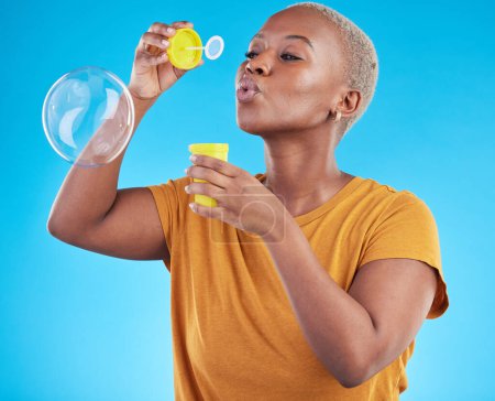 Photo for African, woman and blowing bubbles in studio, blue background or fun party celebration with liquid soap or toy. African girl, person and relax with happy, joyful or creative bubble for calm break. - Royalty Free Image