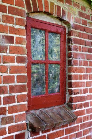 Photo for Old dirty window in a brick wall house or home. Ancient casement with red wood frame on a historic building with a clumpy paint texture. Exterior details of a windowsill in a traditional country town. - Royalty Free Image