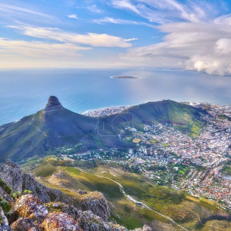 Téléchargez les photos : Vue aérienne du paysage de Lions Head et des environs à Cape Town, en Afrique du Sud. Repère naturel pittoresque d'une montagne populaire contre un ciel bleu nuageux dans une belle ville urbaine d'en haut. - en image libre de droit