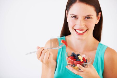Téléchargez les photos : Nourriture, salade de fruits et portrait de femme souriante mangeant pour la nutrition, le bien-être et la collation aux baies en studio. Santé, heureux et visage de la personne pour les vitamines, l'alimentation et perdre du poids sur fond blanc. - en image libre de droit
