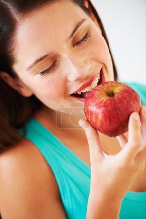 Téléchargez les photos : Santé, alimentation et visage de la femme mangeant des pommes pour la nutrition, le bien-être et la collation en studio. Nourriture, heureux et personne avec des fruits pour les vitamines, les avantages de désintoxication et de perdre du poids sur fond blanc. - en image libre de droit