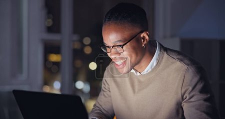 Téléchargez les photos : Homme d'affaires, nuit et ordinateur portable avec le sourire au bureau, la lecture d'e-mail avec des progrès de carrière dans l'entreprise. Homme noir, lunettes et ordinateur pour heureux dans le travail à distance, focus et recherche Internet pour la stratégie. - en image libre de droit