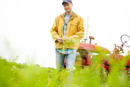 Foto de Sólo somos mi tractor y yo. Retrato de un granjero parado en un campo con su tractor aparcado detrás de él - Copyspace - Imagen libre de derechos