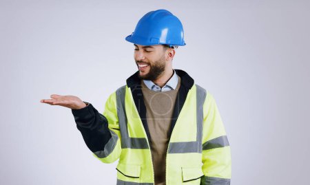 Photo for Happy man, architect and palm for advertising or marketing against a gray studio background. Male person, contractor or engineer smile with hard hat and hand out for deal or service in construction. - Royalty Free Image