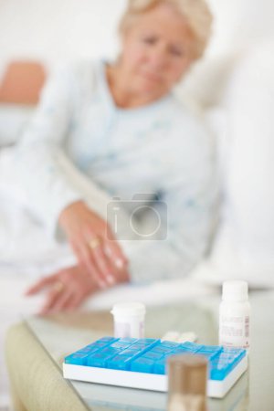 Foto de Dosis diaria - Senior Health. Primer plano de una dosis médica diaria con la mujer alcanzando para ella borrosa en el fondo - Imagen libre de derechos