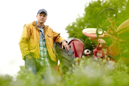 Foto de Listo para otro día en los felds. Retrato del granjero guapo apoyado en el neumático de su tractor en un campo - Imagen libre de derechos