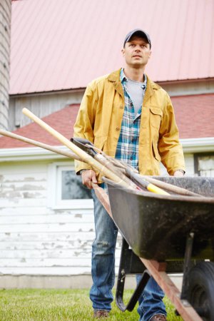 Photo for I work hard. A serious man standing outside with his wheelbarrow - Royalty Free Image