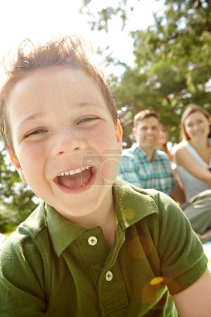 Téléchargez les photos : Il riait toujours vite et souriait. Un petit garçon heureux assis à l'extérieur avec sa famille par une journée ensoleillée - en image libre de droit
