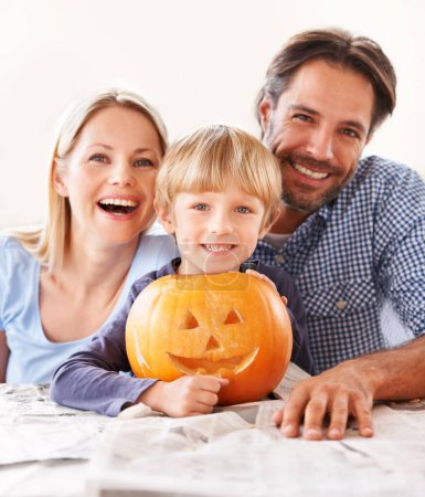 Téléchargez les photos : Une famille frappant leur Jack-o-lantern. Portrait d'un mari et d'une femme avec leur fils derrière une citrouille sculptée pour Halloween - en image libre de droit
