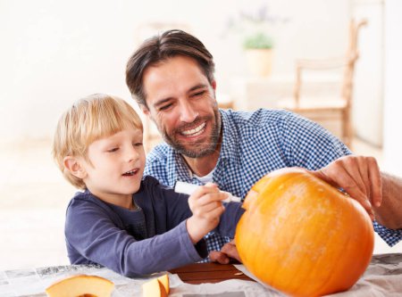 Foto de Espera, una última cosa. Un padre y un hijo marcando una calabaza en casa para Halloween - Imagen libre de derechos