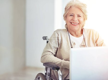 Téléchargez les photos : Jeune de cœur... un peu plus âgé ailleurs. une femme âgée utilisant un ordinateur portable assis dans un fauteuil roulant - en image libre de droit
