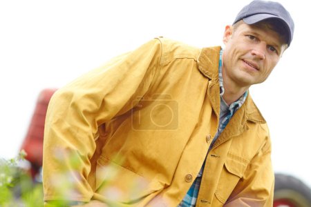 Téléchargez les photos : Le style de vie d'un vrai fermier. Portrait d'un agriculteur agenouillé dans un champ avec son tracteur garé derrière lui - en image libre de droit