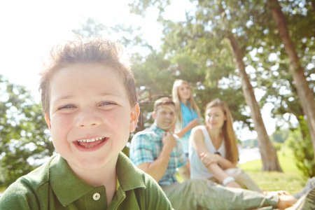 Téléchargez les photos : Il adore passer du temps avec sa famille. Un petit garçon heureux assis à l'extérieur avec sa famille par une journée ensoleillée - en image libre de droit