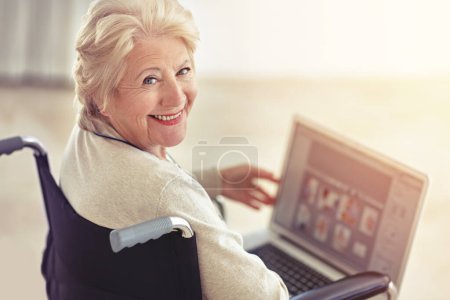 Téléchargez les photos : C'est une terminale douée en technologie. une femme âgée utilisant un ordinateur portable assis dans un fauteuil roulant - en image libre de droit