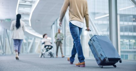 Photo for Closeup, walking and man with a suitcase, back and airport to travel, vacation or holiday in airline hallway. Luggage, legs and person on flight terminal, immigration journey or international trip. - Royalty Free Image