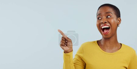 Téléchargez les photos : Heureuse femme noire, pointant et surprise pour la publicité ou le marketing sur un fond de studio gris. Visage de femme africaine excitée sourire dans wow deal, promotion de vente ou réduction sur la maquette. - en image libre de droit