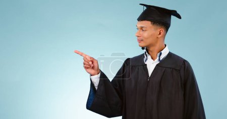 Photo for Education, graduation and a student man pointing to space in studio on a blue background for marketing. School, university or college with a confident young graduate on mockup for advertising. - Royalty Free Image