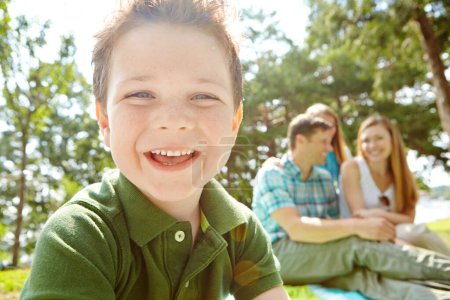 Téléchargez les photos : Profiter du temps en famille dans le parc. Un petit garçon heureux assis à l'extérieur avec sa famille par une journée ensoleillée - en image libre de droit