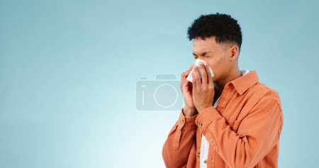 Foto de Hombre, sonando y la nariz para los senos paranasales en el estudio para la atención médica se burlan de fondo azul en Ciudad del Cabo. Modelo masculino, mano y tejido para fiebre del heno, gripe o congestión para alergias con anuncio en el espacio. - Imagen libre de derechos