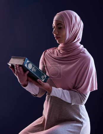 Téléchargez les photos : Coran, foi et femme musulmane lisant dans un studio avec vêtements traditionnels et hijab. Sérieux, religion et jeune musulmane étudiant le saint livre arabe isolé par un fond noir - en image libre de droit