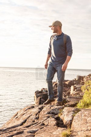 Foto de Me encontré con algunos lugares de interés mientras caminaba. un hombre vistiendo su mochila mientras estaba fuera para una caminata en un sendero costero - Imagen libre de derechos