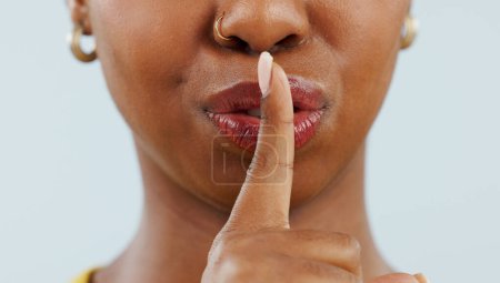 Foto de Mujer negra, boca y labios en secreto para chismes, privacidad o información confidencial en un fondo de estudio. Primer plano de la mujer africana con el dedo o emoji en silencio, silencio o susurro. - Imagen libre de derechos