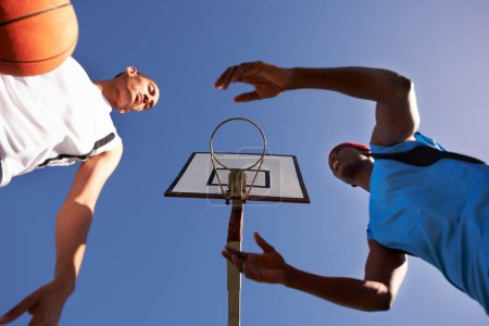 Téléchargez les photos : Hommes, joueur et match de basket-ball au court extérieur ou sous l'angle de l'équipe de défi, dunk sur rival. Hommes, cerceau et point de score dans le parc d'été au jeu de remise en forme ou de compétition, athlète sur ciel bleu. - en image libre de droit