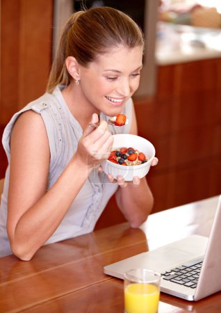Photo for Laptop, happy and woman with fruit breakfast in home for website, internet and reading news blog. Smile, morning and person on computer for connection, networking and streaming service in kitchen. - Royalty Free Image