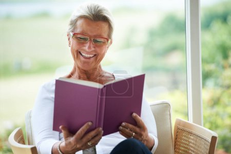 Photo for Senior woman, home and book with reading, chair or relax in living room with smile for story, knowledge or glasses. Happy elderly lady, person and thinking in lounge in retirement with novel in house. - Royalty Free Image