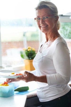 Photo for Senior, woman and portrait dish vegetables for lunch meal for holiday food, retirement relax in home. Female person, face and smile for eating healthy vitamin or nutrition, kitchen counter at brunch. - Royalty Free Image