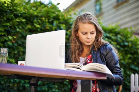 Photo for Woman, book and laptop by cafe outdoors and sitting for reading, assignment or work. Young, female student and technology for online, submission or document for research, project or college test. - Royalty Free Image