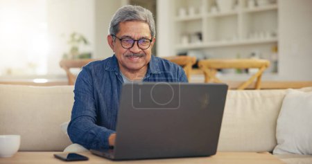 Photo for Elderly, man and smile for laptop living room on sofa for typing, email or message for communication. Senior person, looking at screen and glasses with technology, internet or web for work from home. - Royalty Free Image