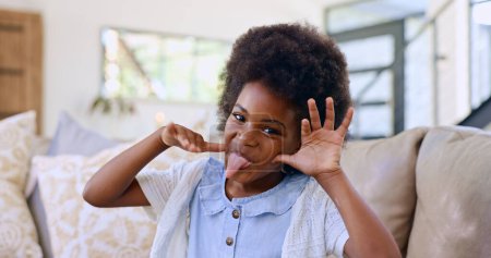 Photo for Funny, face and girl child with tongue out on a sofa for fun, playing or goofy personality at home. Crazy, hand gesture and portrait of African kid in living room with comic expression or silly mood. - Royalty Free Image