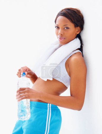 Foto de Mujer negra, agua y botella para fitness en estudio retrato con toalla para entrenamiento, salud o bienestar. Chica africana, ejercicio y ejercicio con bebida para la hidratación, desintoxicación y líquido para la rutina de gimnasia. - Imagen libre de derechos