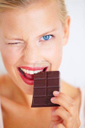 Photo for Portrait, woman wink and eating chocolate bar, delicious snack or candy for studio food, dessert or sugar product. Diet craving, cacao sweets or girl face with cheat meal isolated on white background. - Royalty Free Image
