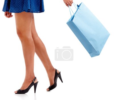 Foto de Mujer, piernas y bolsa de compras en tacones altos para la moda aislada sobre un fondo de estudio blanco. Mujer persona, comprador o modelo caminando con regalo, regalo o descuento de venta en la compra de ropa. - Imagen libre de derechos