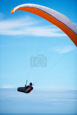Photo for Man, paragliding and blue sky adventure parachute in clouds for explore city, outdoor courage or fearless athlete. Male person, safety equipment for landing flying in nature sport, activity in wind. - Royalty Free Image