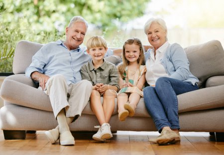 Téléchargez les photos : Heureux, portrait et enfants avec grands-parents sur un canapé dans le salon de la maison familiale moderne. Sourire, amour et jeunes enfants assis avec grand-père et grand-mère sur le canapé dans le salon à la maison - en image libre de droit