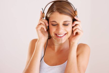 Photo for Woman, music and smile with headphones in studio for freedom, audio subscription and streaming multimedia album on white background. Face of happy model listening to podcast, hearing sound and radio. - Royalty Free Image