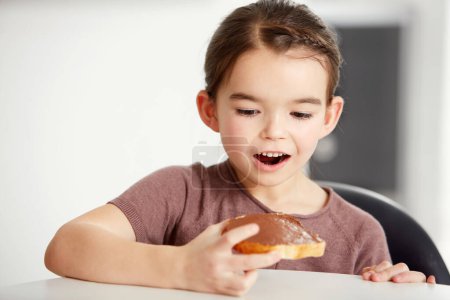 Photo for Little girl, toast and chocolate spread for sweet, delicious or desert snack on bread in kitchen at home. Young female person, child or kid in surprise for food or candy treat on wheat at house. - Royalty Free Image