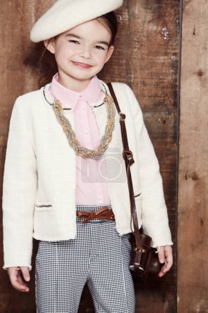 Photo for Vintage, girl and portrait of child with fashion, style and happy in clothes on wood background or studio. Kid, smile and confidence in retro aesthetic or costume with hat, jewellery and bag. - Royalty Free Image