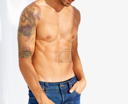 Photo for Fashion, tattoo and shirtless with a man outdoor on a white background for edgy or unique style. Health, fitness and denim jeans with the body of a model in the sunlight for masculine or macho style. - Royalty Free Image