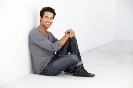 Photo for Smile, fashion and portrait of young man by a white wall in empty room with casual, cool and trendy outfit. Happy, confidence and handsome male model from Canada sitting on floor with edgy style - Royalty Free Image