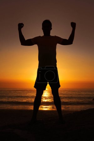 Photo for Silhouette, man and flex with sunset for winner, health and wellness on beach with sunrise and zen. Person, shadow and pilates or celebration for victory, mindfulness and healthy body by ocean or sea. - Royalty Free Image
