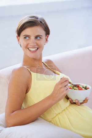 Foto de Mujer embarazada, ensalada y feliz en sofá para la salud, la nutrición y el bienestar en la sala de estar del apartamento. Persona, verduras o sonrisa en el sofá del salón para relajarse, embarazo y dieta saludable con fibra. - Imagen libre de derechos