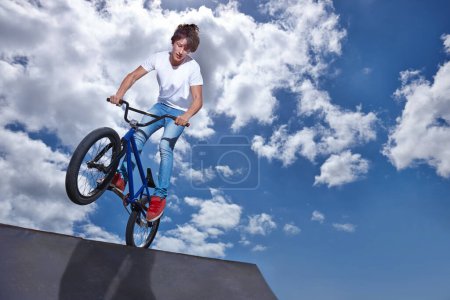 Foto de Equitación, bicicleta y adolescente en rampa para el rendimiento deportivo, salto o entrenamiento para el evento en el parque con maqueta cielo azul. Bicicleta, truco o equilibrio infantil en el borde de la tabla en el truco para el desafío de la competencia ciclista. - Imagen libre de derechos