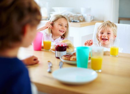Foto de Feliz, cocina y niños desayunando juntos para una comida saludable, de bienestar y dieta. Sonríe, ríe y los hermanos pequeños se unen y disfrutan de un almuerzo o brunch junto a una mesa de madera en la casa familiar moderna - Imagen libre de derechos